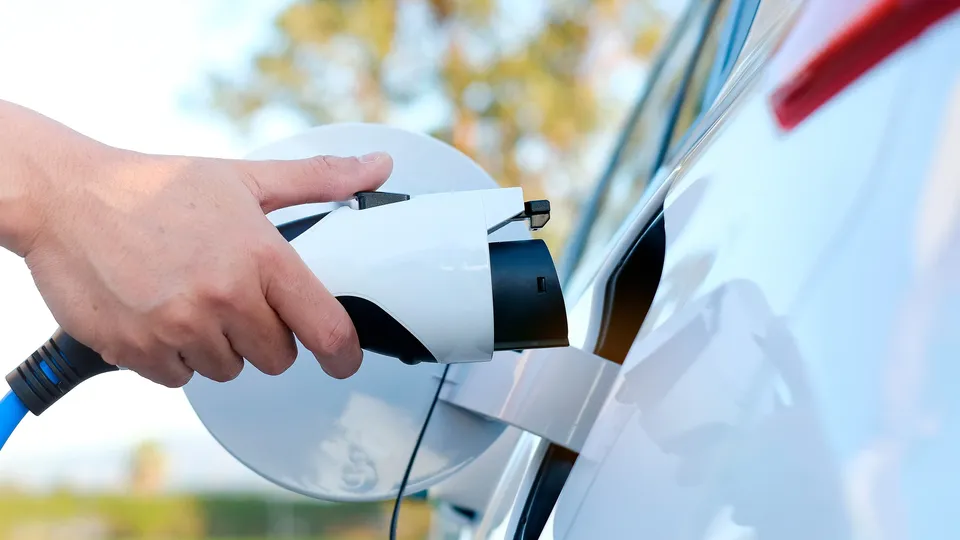 Mão segurando conector de carregamento de veículo elétrico perto da porta de carregamento do carro.