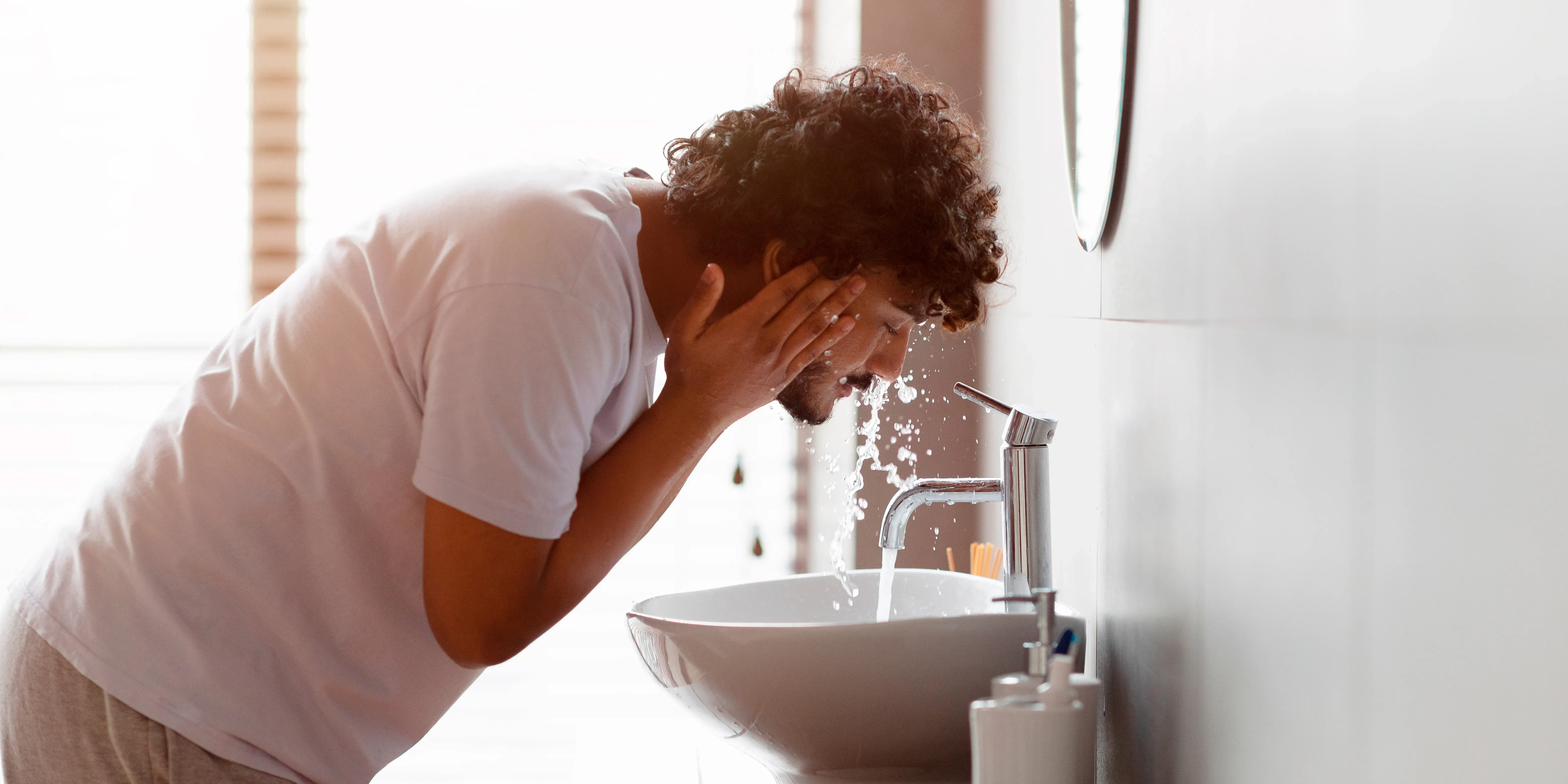 Hombre lavándose la cara en el lavabo del baño con agua corriente.