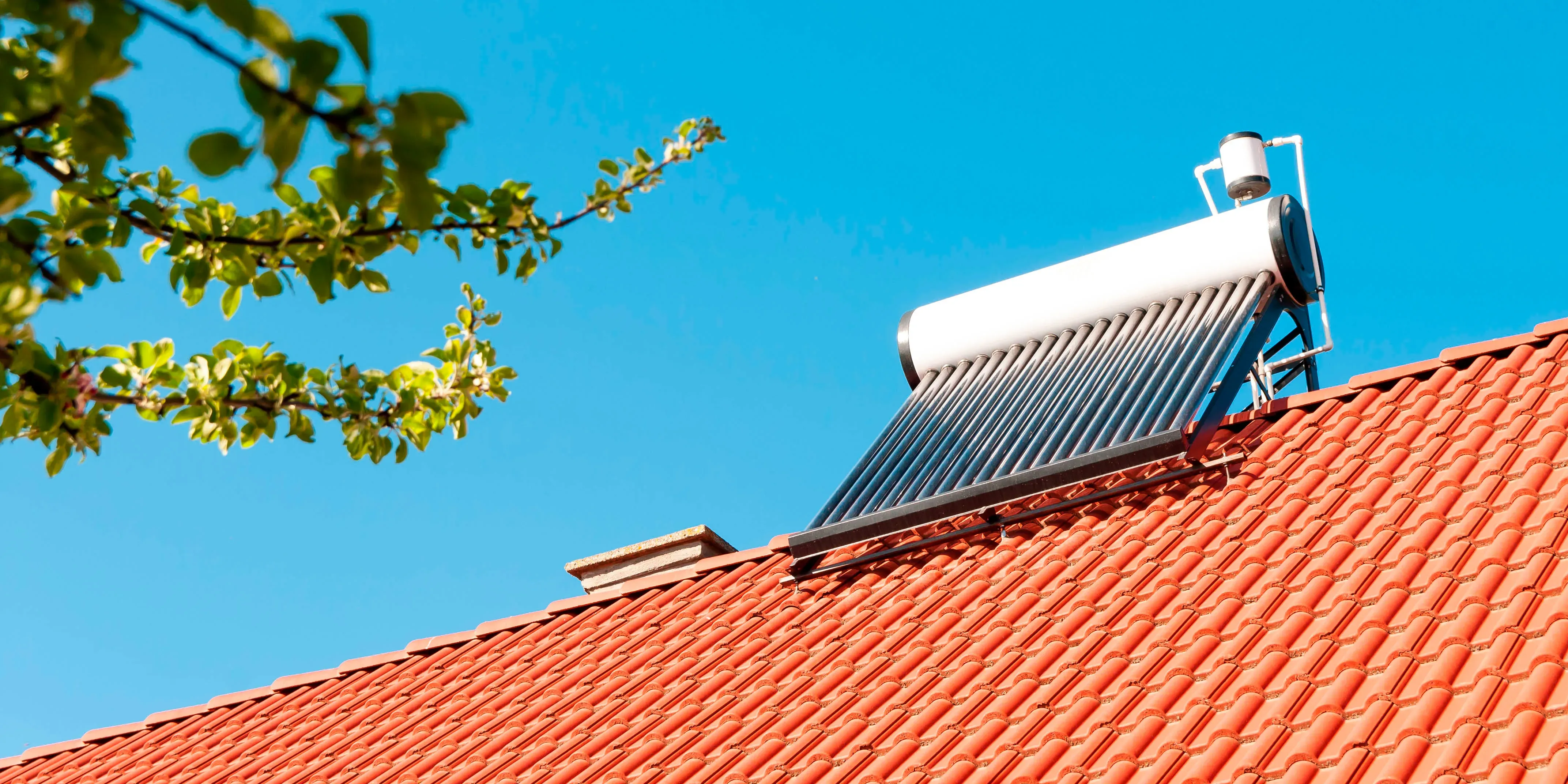 Calentador solar de agua instalado en techo de tejas rojas bajo cielo despejado.