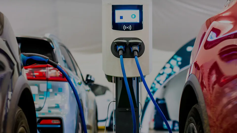 Elektrisk køretøjsopladningsstation med to blå kabler forbundet til parkerede biler.