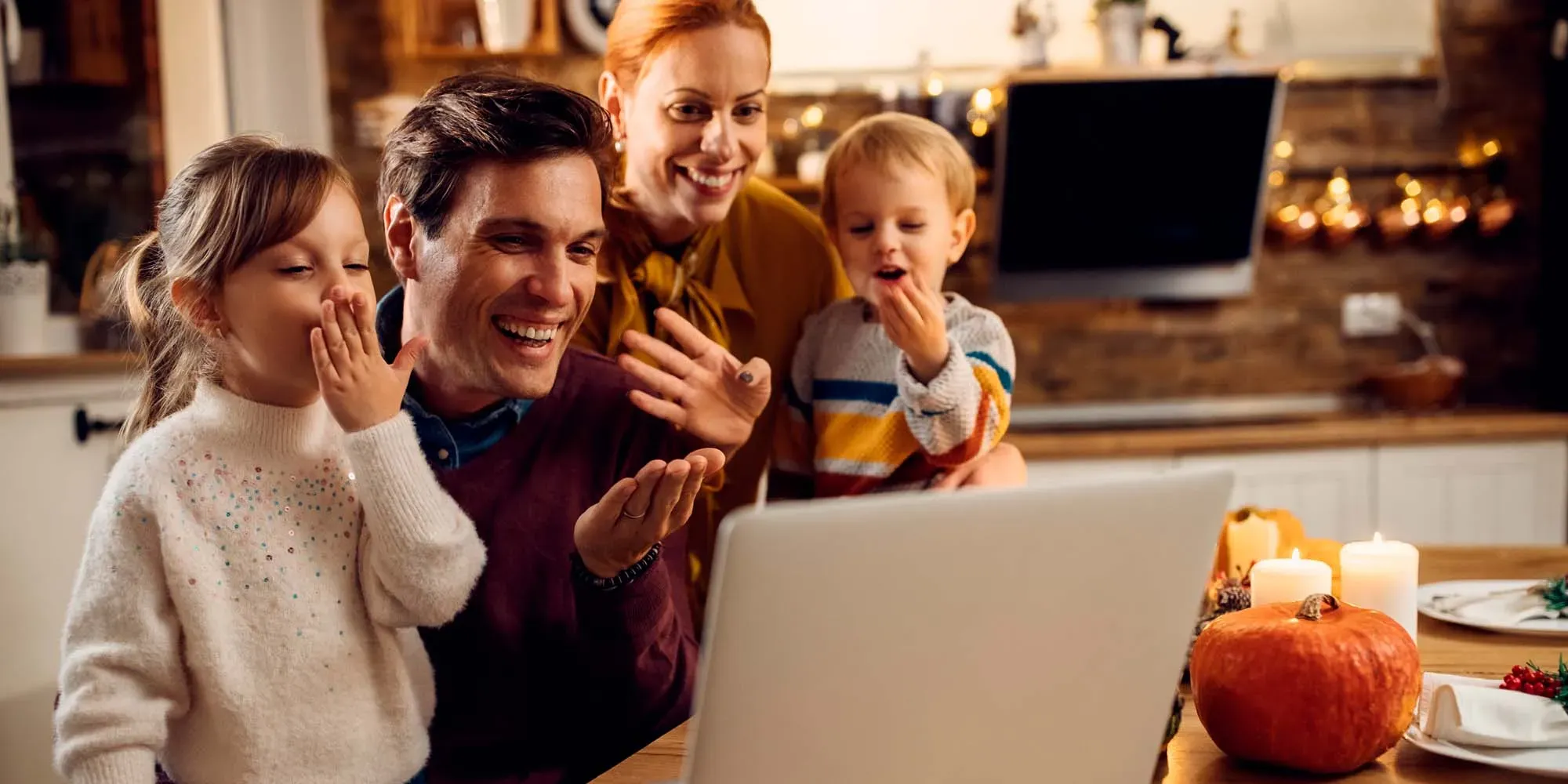 Familia de cuatro personas reunidas alrededor de un portátil, sonriendo y señalando la pantalla.
