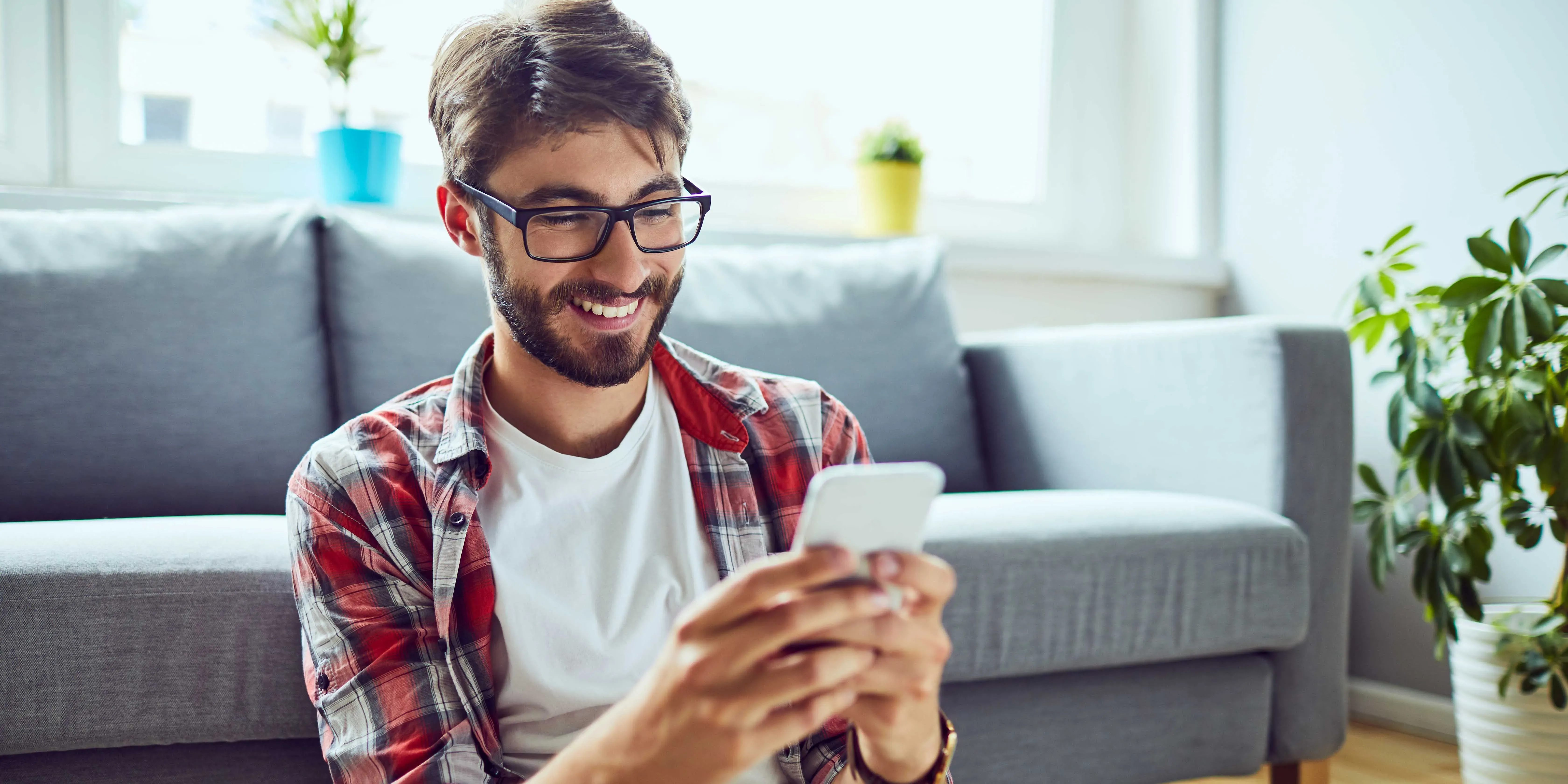 Hombre sonriendo mientras mira un smartphone en el sofá.