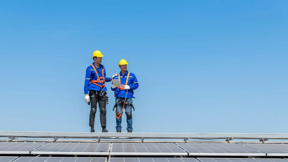 Two construction workers on solar panels reviewing documents.