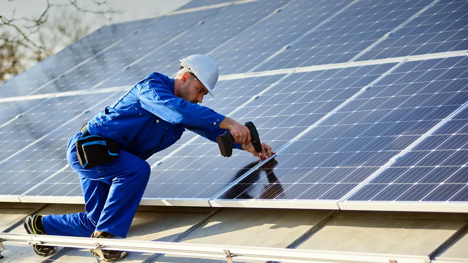 Instalador de paneles solares clavando riel de montaje en paneles de techo.