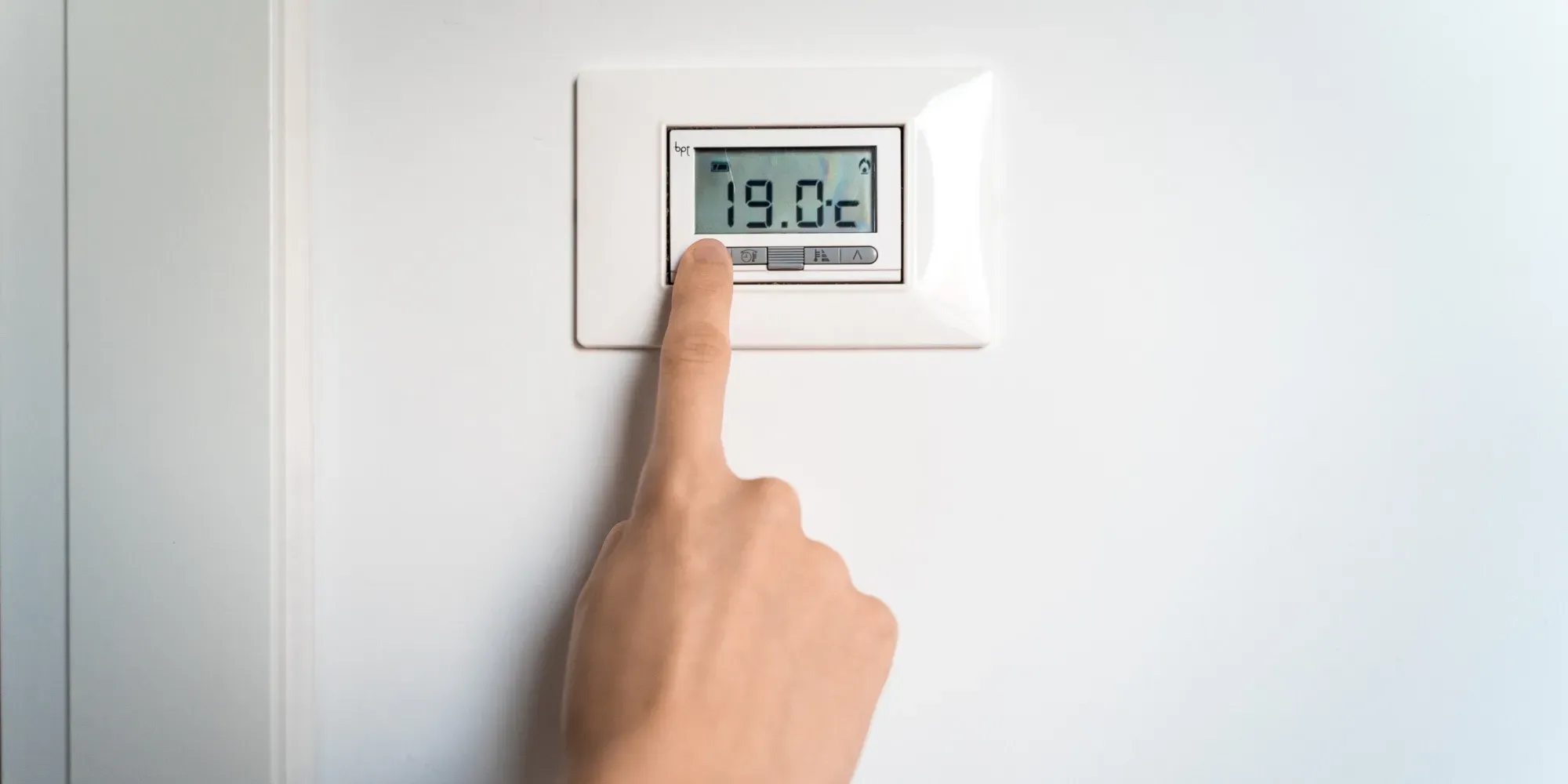 Person pointing at digital thermostat displaying 19.0 degrees Celsius.