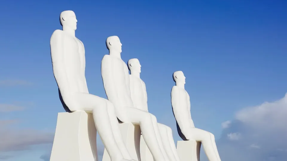 Fire hvide siddende figurer med blå himmel i baggrunden.