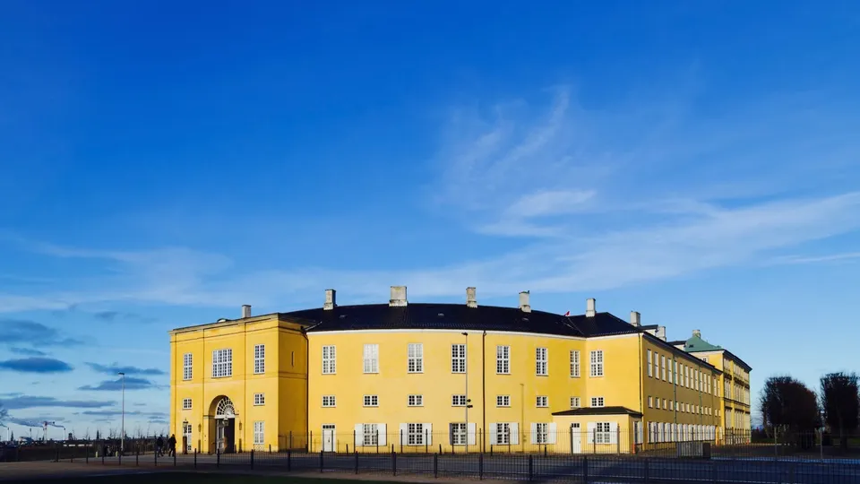 Lysegult bygning med sort tag og flere vinduer med blå himmel.