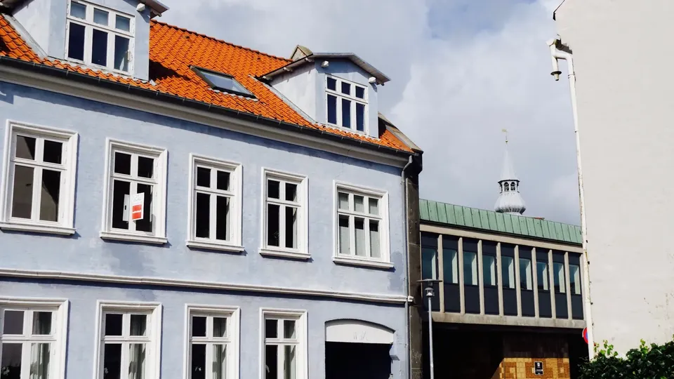 Blåmalet historisk bygning med rødt tegltag og hvide vinduesrammer.
