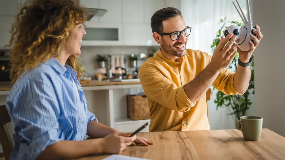 Hombre sosteniendo una manualidad decorativa de búho mientras una mujer observa en la mesa de la cocina.