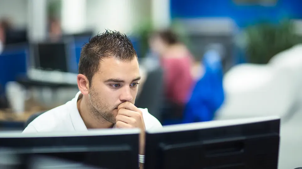 Hombre concentrado en el monitor de su ordenador en un entorno de oficina.