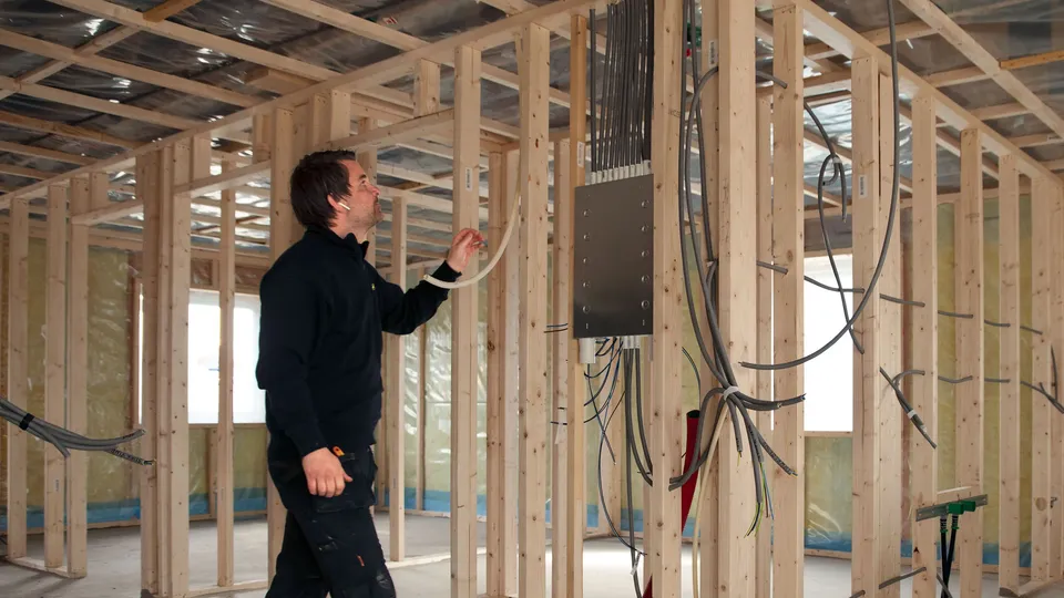 Elektriker installerer ledninger i tømmerkonstruksjon under bygging.