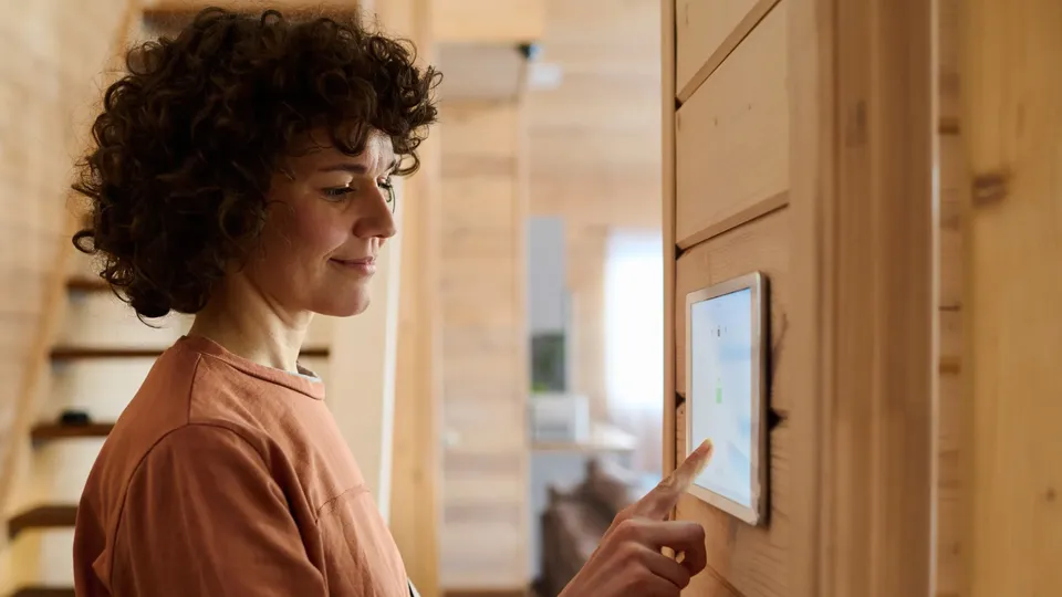 Mujer tocando un panel de control de casa inteligente en la pared.