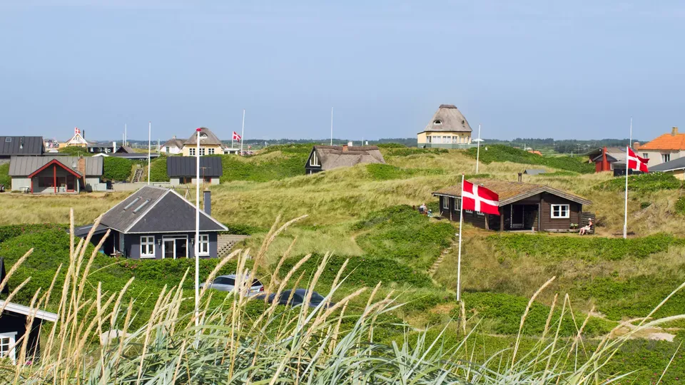 Dansk kystby med huse med stråtag og danske flag i græsbevokset klit.