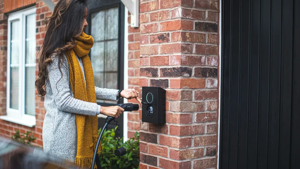 Woman using electric vehicle charging station at home.
