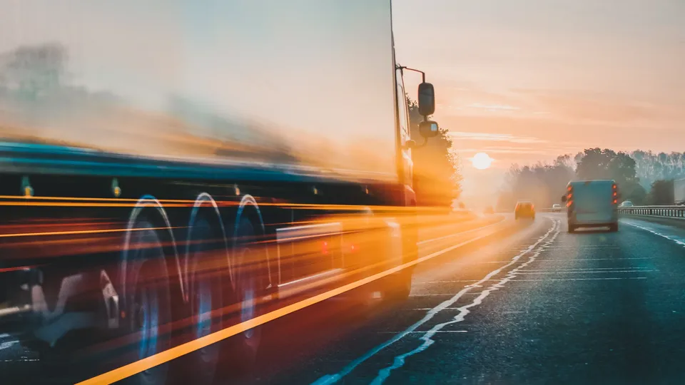 Lastbiler kører på motorvej ved solnedgang.