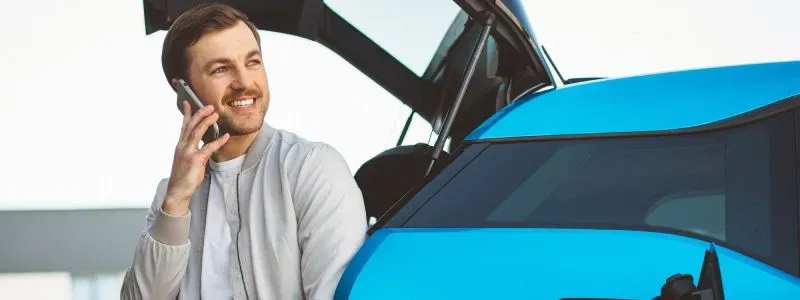 Uomo al telefono accanto a auto blu con cofano aperto.