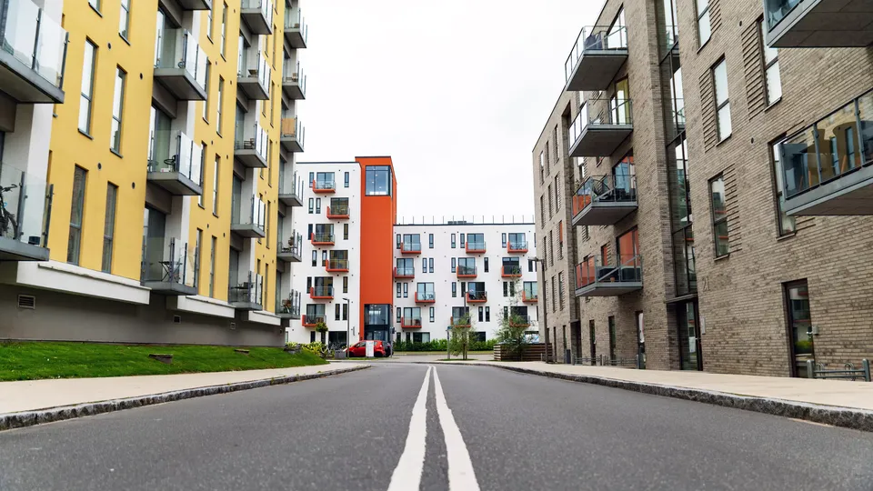 Billede af Aalborg: Vej med hvid midterlinje fører mod moderne lejlighedsbygninger.