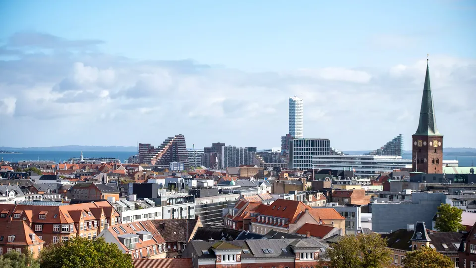 Byudsigt over Aarhus med historiske røde tage og moderne skyskrabere ved vandkanten.