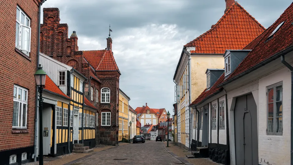 Billede af Midtjylland: Brolagt gade omgivet af farveflade historiske bygninger med røde tegltage.