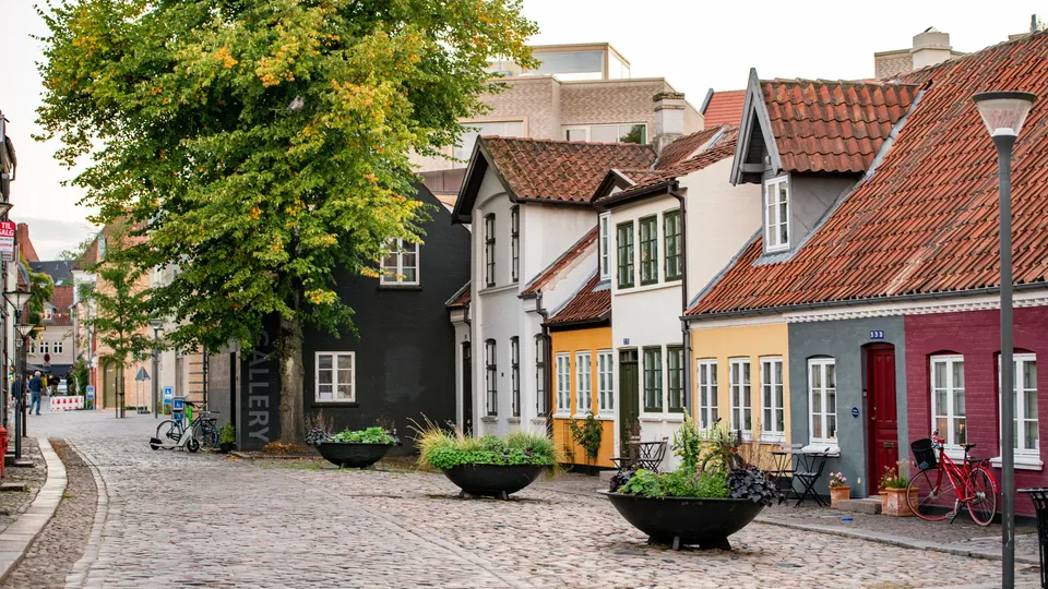 Billede af Odense: Farvefulde rækkehuse langs en brostensgade på et europæisk torv.