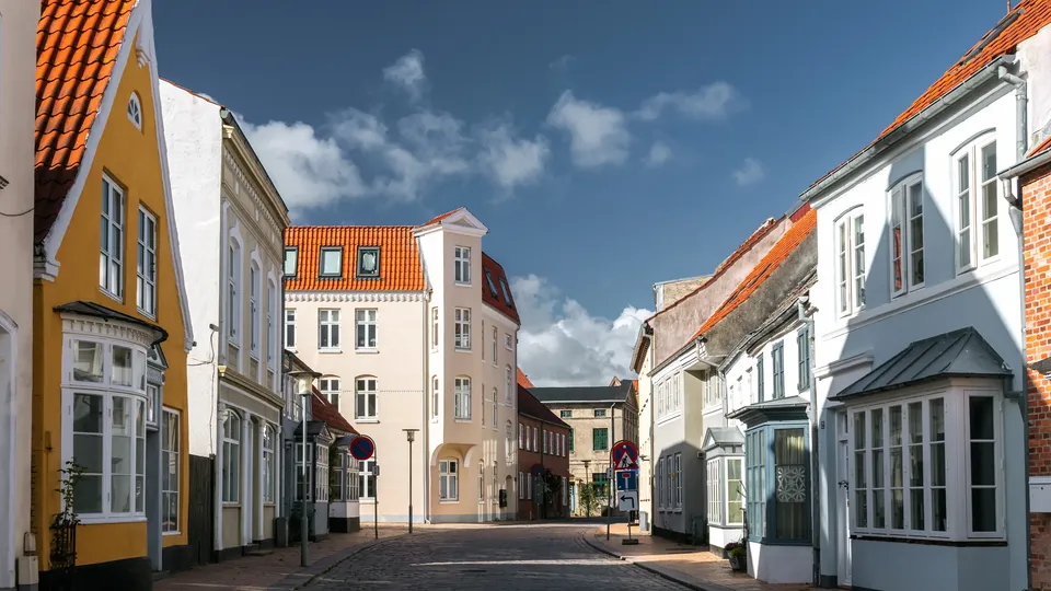 Billede af Sønderjylland: Brostensgade omgivet af farvede historiske bygninger under blå himmel.