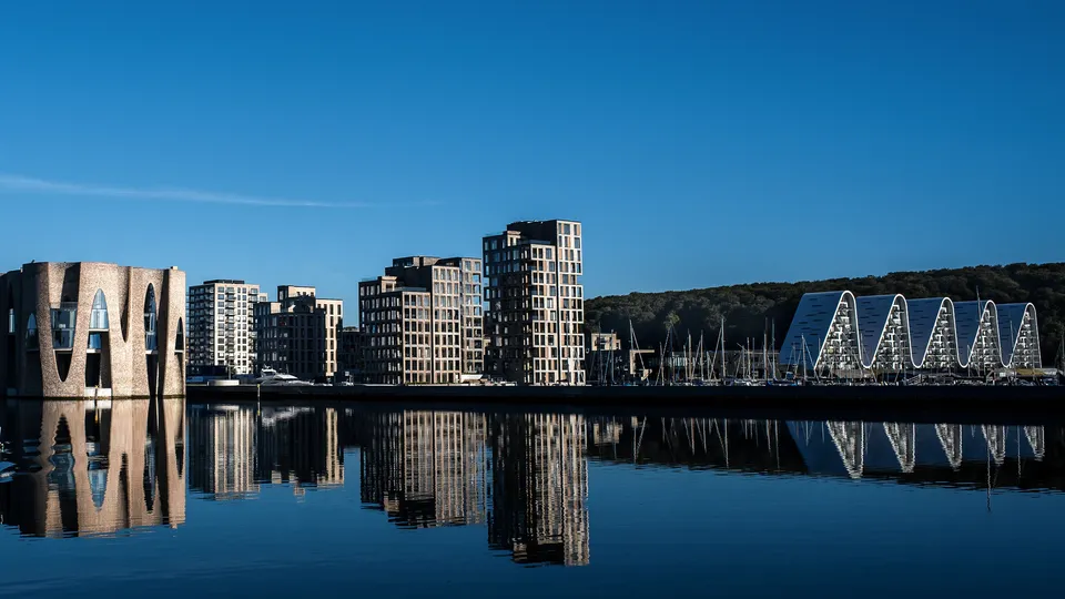 Billede af vejle: Moderne bybillede ved vandet, hvor bygninger bliver reflekteret i blåt vand.
