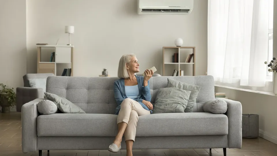 Woman sitting on her couch with air air heat pump on the wall