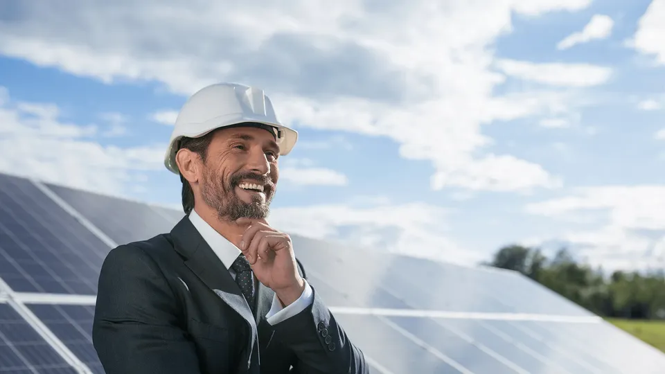 Uomo d'affari con casco che sorride davanti a pannelli solari.