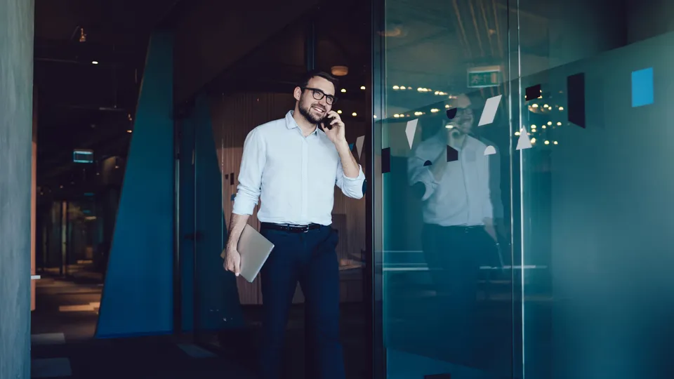 Eiendomsmegler i telefonsamtale som holder PC på kontor.