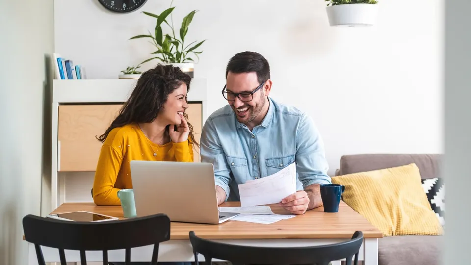 Uomo e donna gestiscono le finanze sorridendo al tavolo della cucina