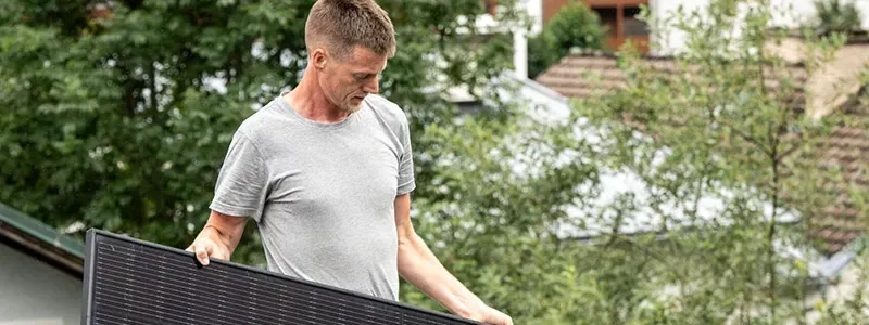 DAFi GmbH – Monteur trägt Photovoltaik-Solarmodul auf Hausdach im Grünen