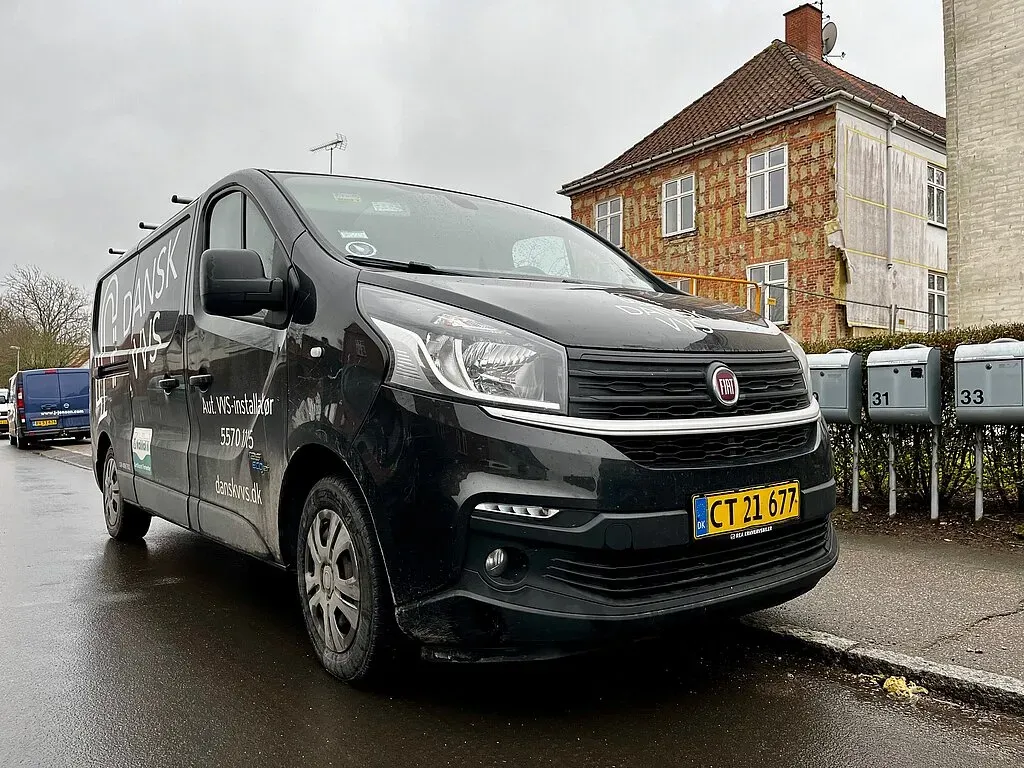 Sort arbejdskørretøj parkeret foran murstensbygning.
