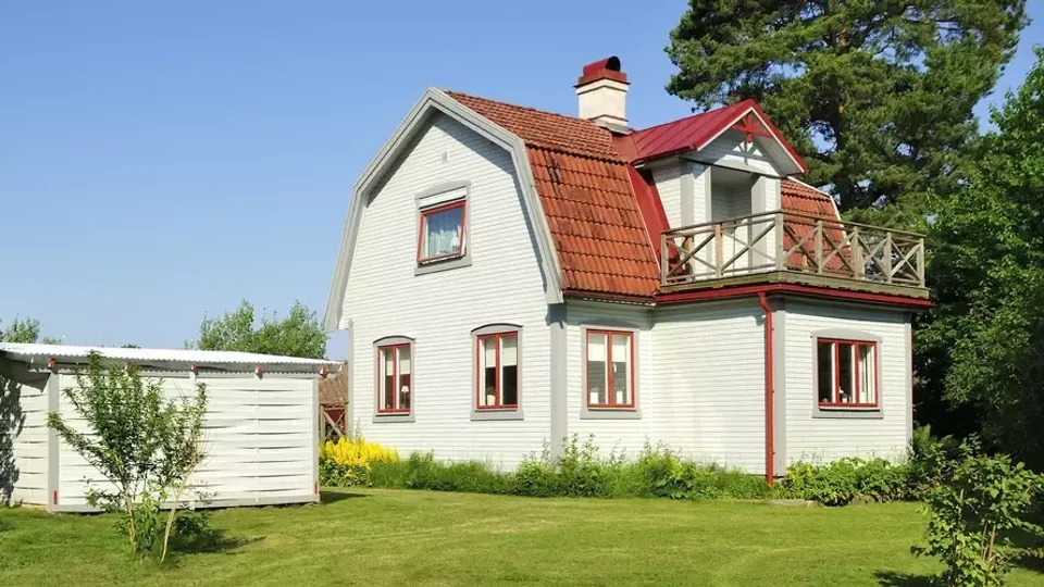Vitt hus med rött tak och balkong omgivet av grön gräsmatta.