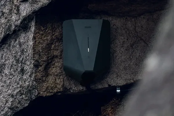 Eine moderne und schwarze E-Ladestation hängt an einem Felsen.