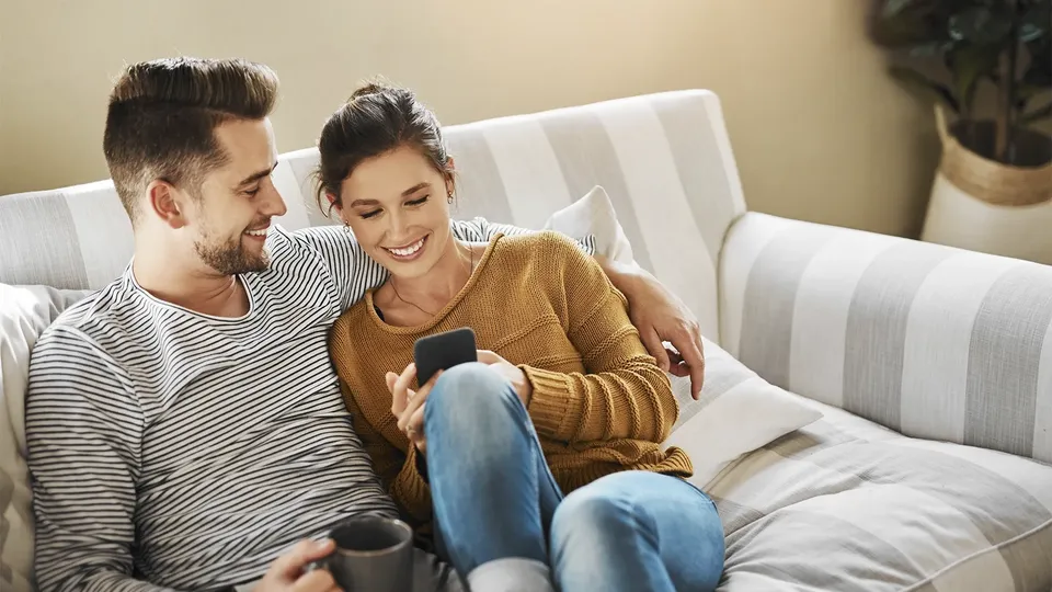 Par på sofa ser sammen på smartphone.