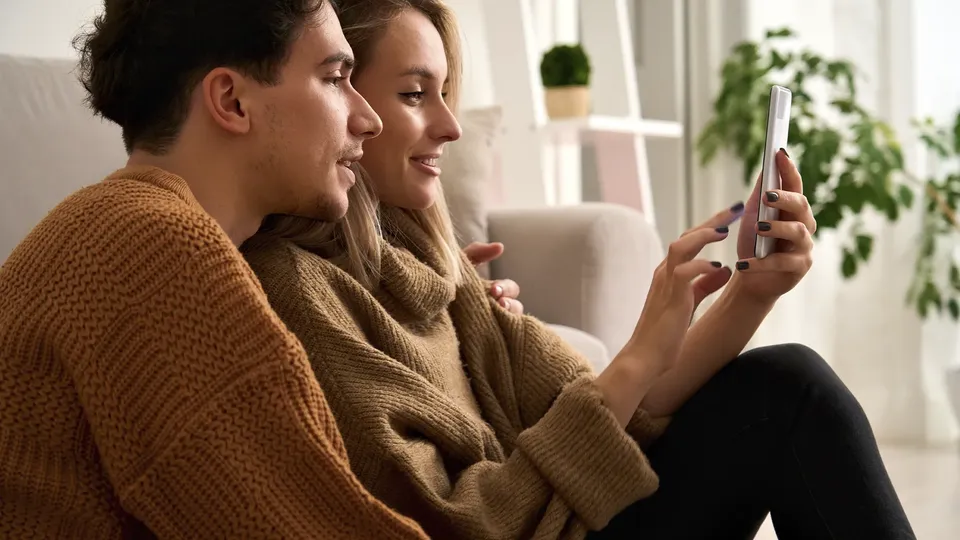 Par smiler mens de ser på smartphone sammen på sofa.