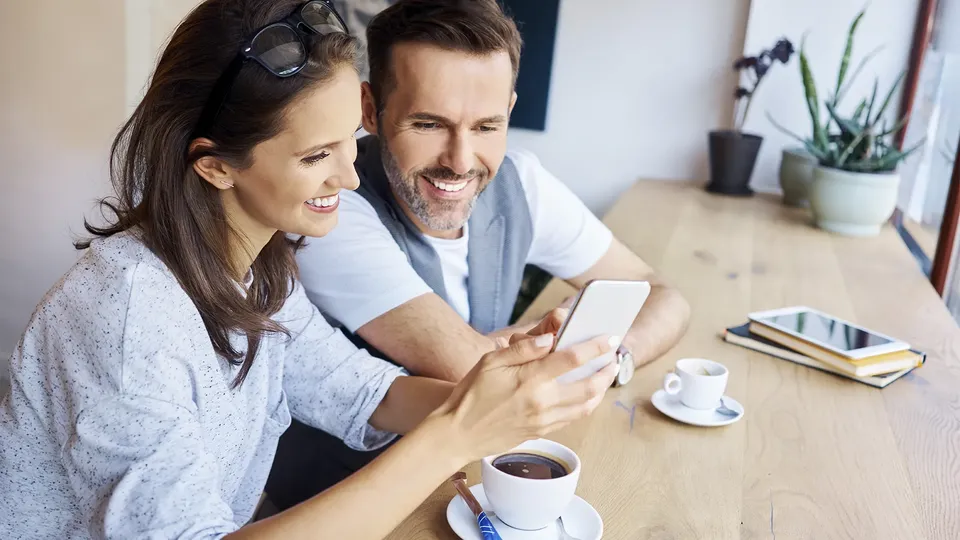 To personer smiler mens de ser på en smartphone sammen ved et bord.