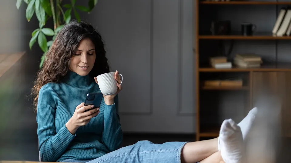 Woman holding coffee mug while looking at smartphone.