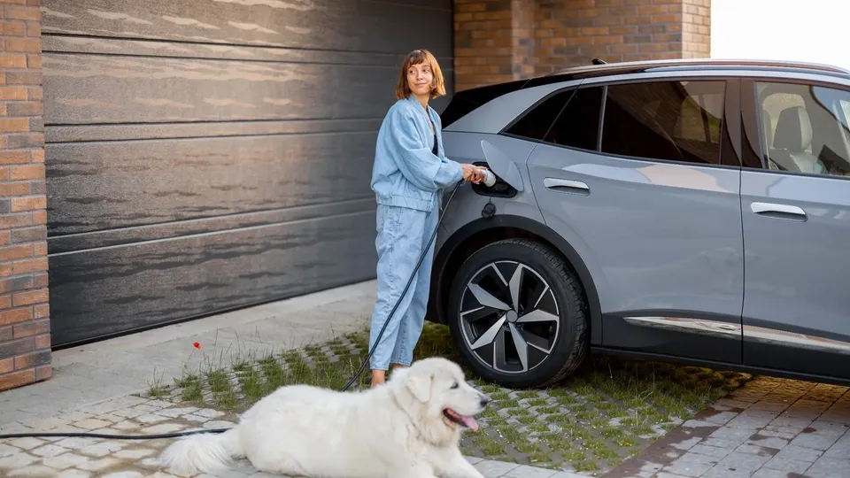 Kvinde lader elbil med hund liggende foran.