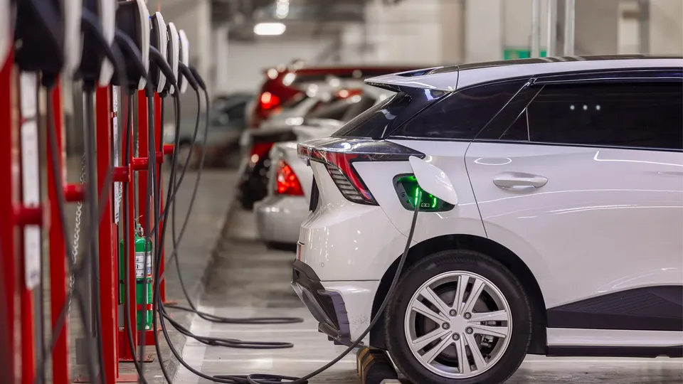 Hvit elektrisk kjøretøy lader ved rød ladestasjonen i parkeringshus.