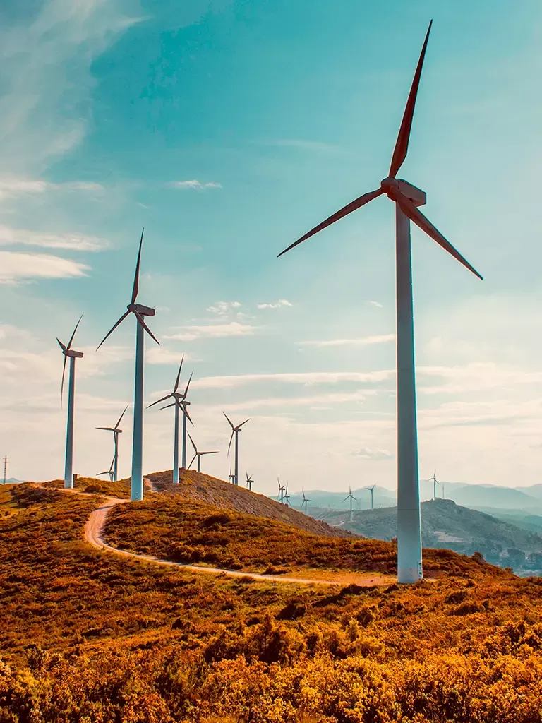 Aerogeradores em encosta com caminho de terra sinuoso pela paisagem.