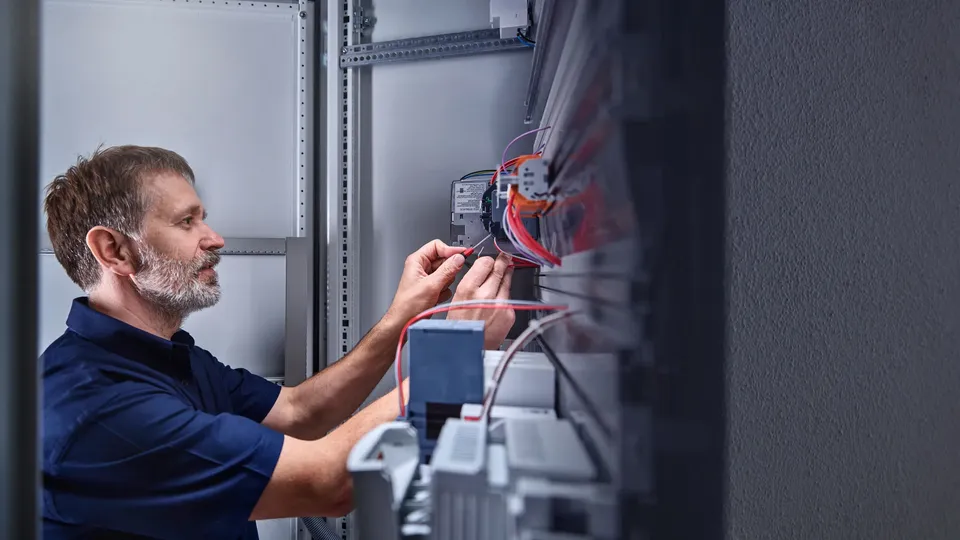 Elektriker arbeider med koblinger i et elektrisk sikringsskap.