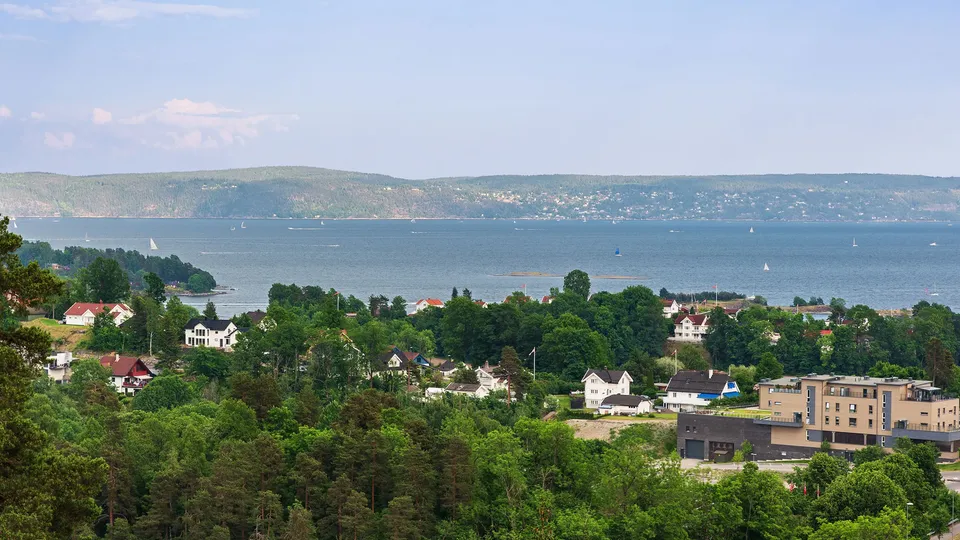 Kystby med hus som overlookerer en fjord med seilbåter og skogkledde åser.