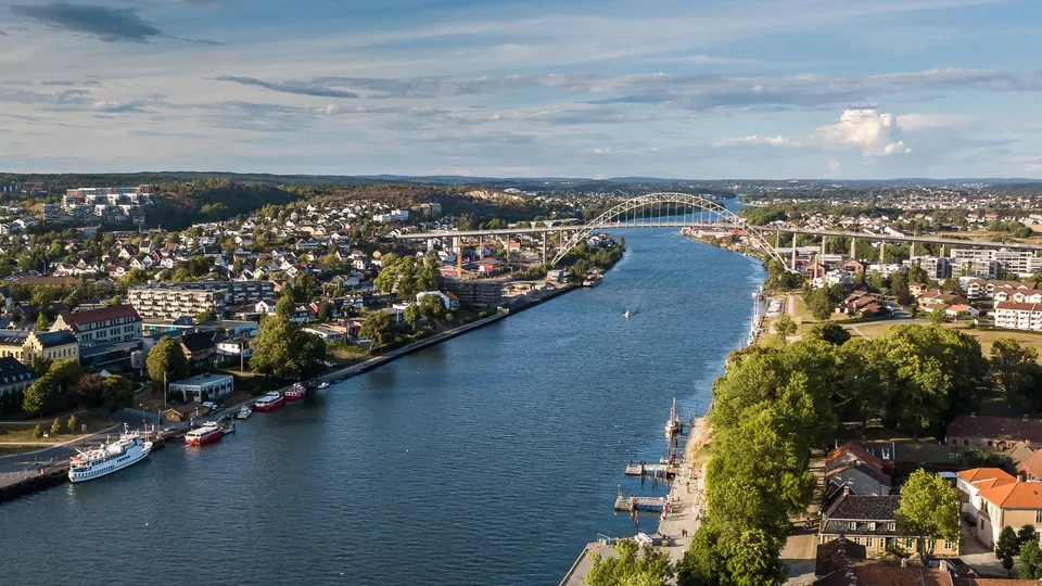 Luftfoto av elv som renner gjennom norsk by med bueformet bru og fortøyde båter.