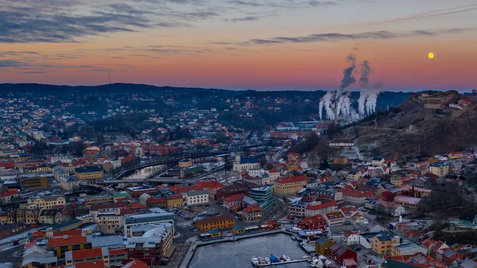 Luftfoto av norsk by i skumringen med elv, bro og industrielle skorsteiner.