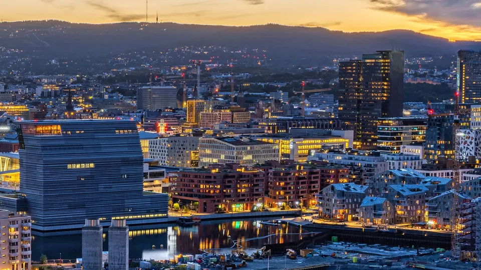 Oslo og Bjørvika i skumringen med opplyste bygninger og vannkant.