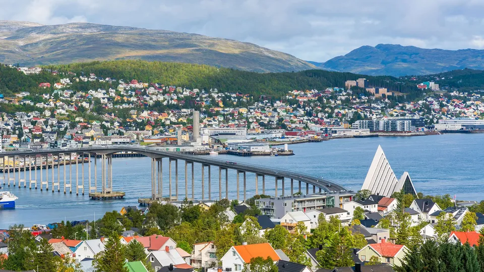 Oversiktsbilde av Tromsø med fargerike hus, bro over blått vann og fjell i bakgrunnen.