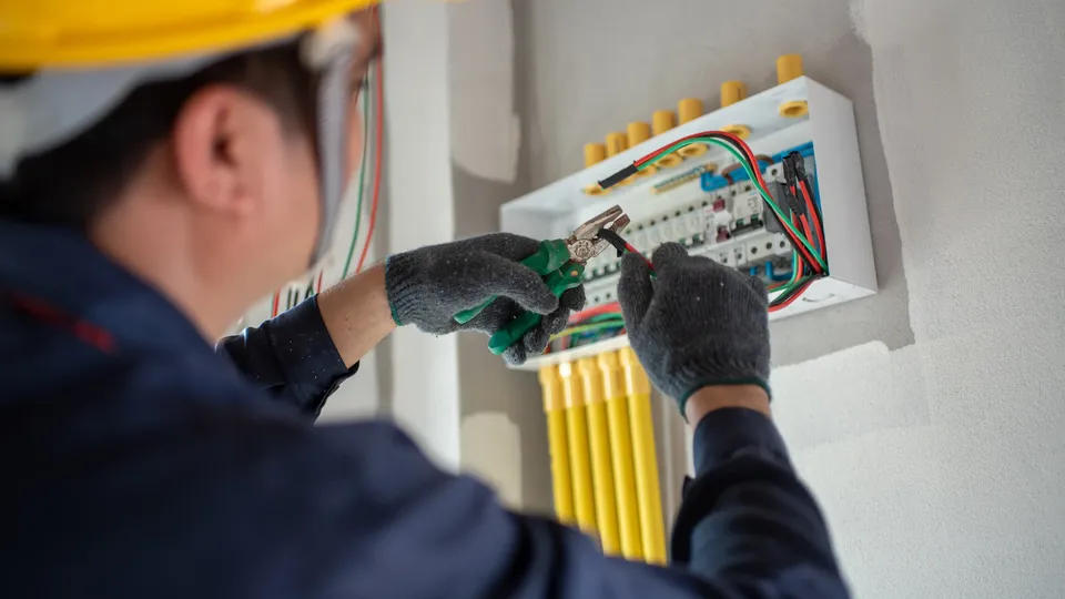 Elektriker mit Schutzhelm arbeitet an Schaltschrankfeld mit farbigen Kabeln.