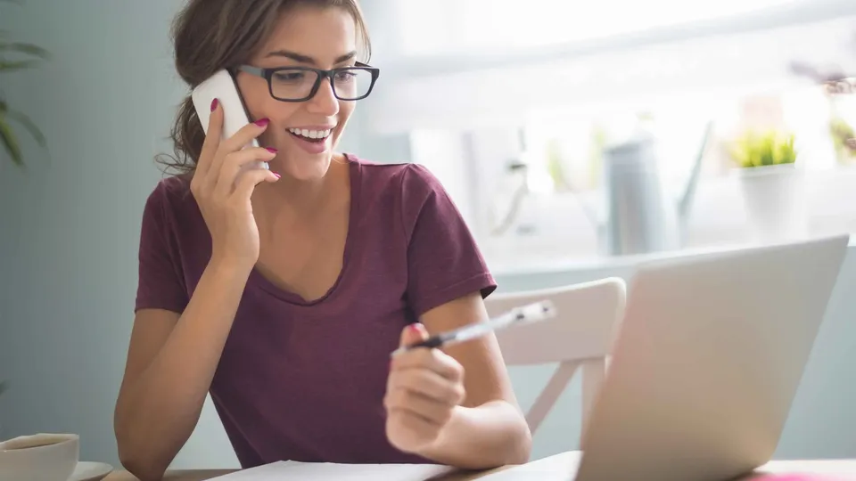 Mulher ao telefone segurando tablet na secretária com portátil.