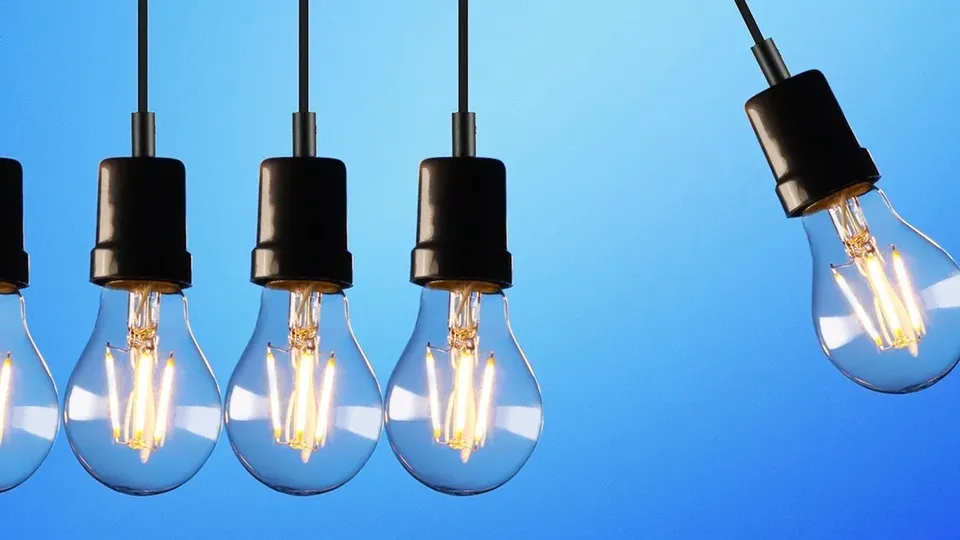 Række af tændte Edison-pærer hængende foran blå baggrund.